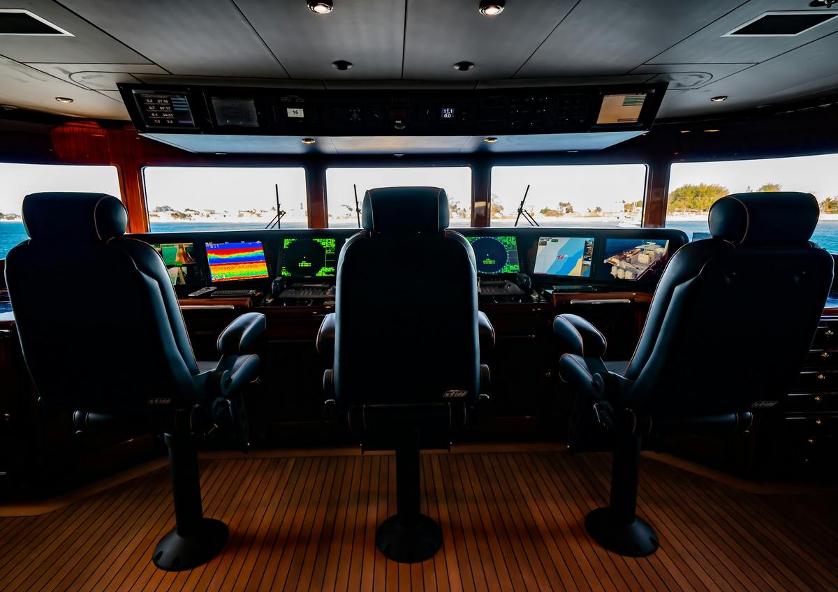 The bridge of a superyacht: three helm chairs facing navigation displays and a teak floor